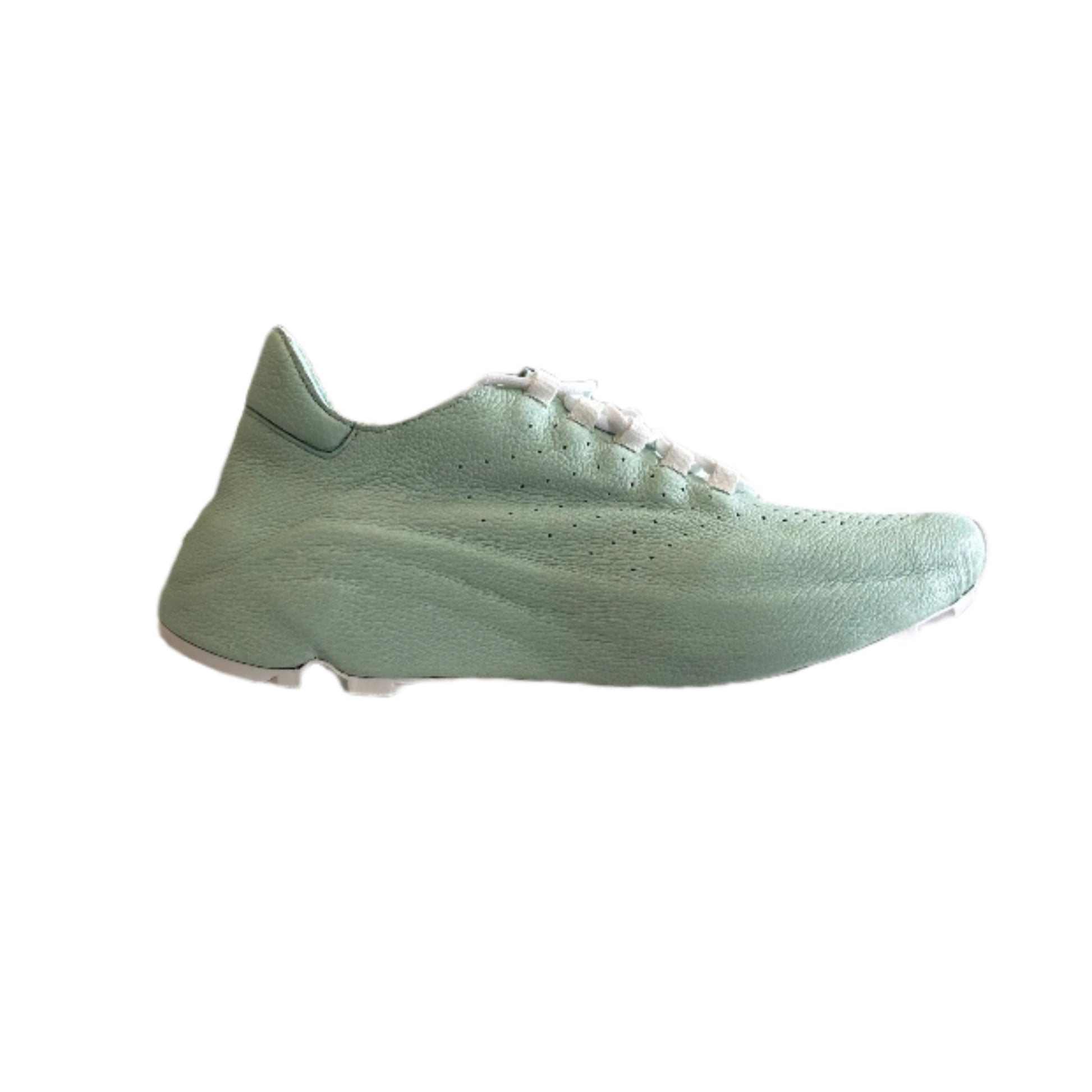 Green sneaker displayed on a stand with clothing items in the background