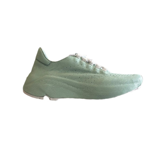 Green sneaker displayed on a stand with clothing items in the background