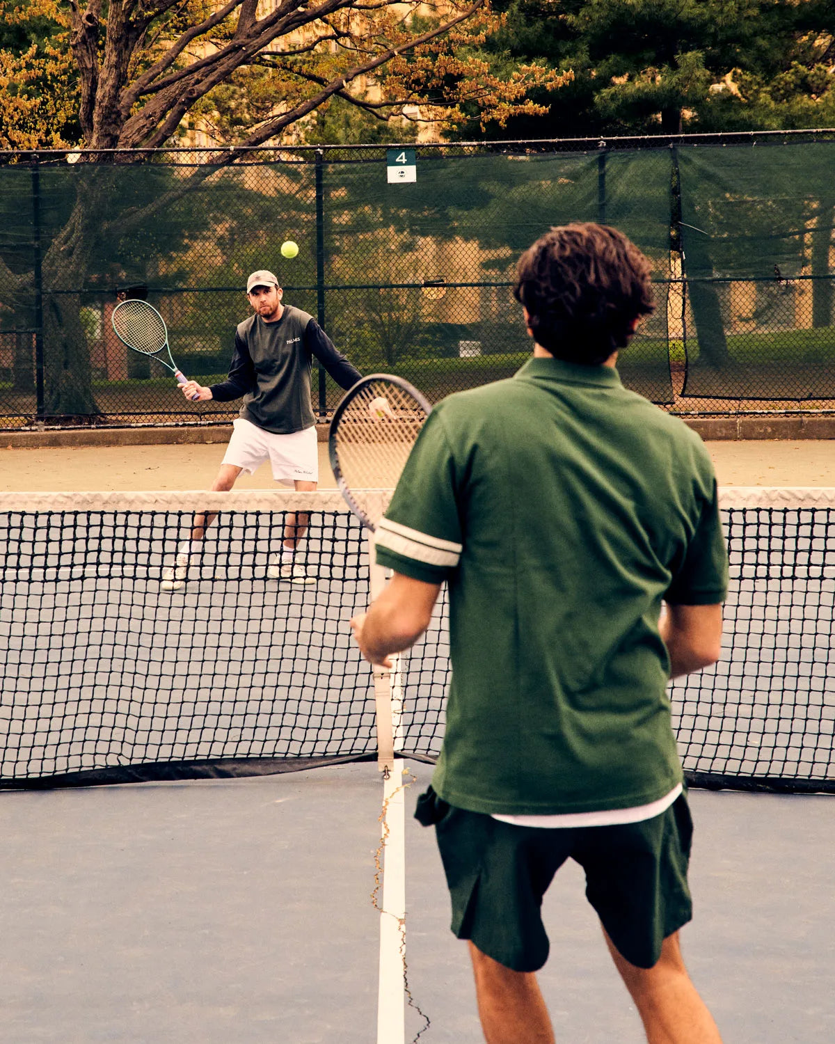 Two men playing tennis on a court with trees in the background